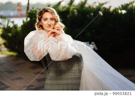 an attractive bride in a white delicate dress on a chair in the park at sunset. an attractive bride in a white delicate dress on a chair in the park at sunset. 99033821