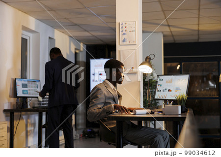 Entrepreneur looking at financial graphs report on computer, planning company investment typing business strategy. African merican executive manager working overhours in startup office 99034612