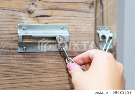 Close up of hand holding security door chain on wooden door Close up of hand holding security door chain on wooden door 99035258
