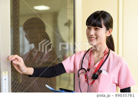 診察室でドアをあけてあげる女性　診療するスクラブを着た笑顔の看護師　医療従事者　医師　外来　診察 99035761