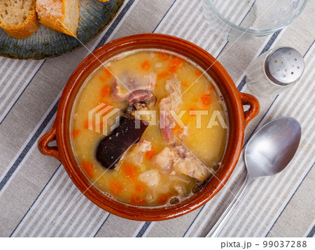 Beautiful serving of pea soup with smoked meat with some bread on side 99037288