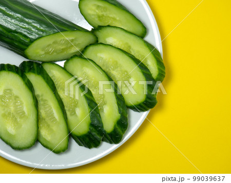 A smooth, medium-sized cucumber on a plate, sliced. Cucumber on a yellow background. 99039637