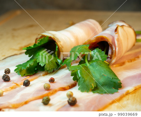 Curvy cut folded into rolls. Pork on a kitchen board with parsley. Still life of meat. Bacon with parsley Curvy cut folded into rolls. Pork on a kitchen board with parsley. Still life of meat. Bacon with parsley 99039669