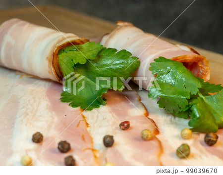 Curvy cut folded into rolls. Pork on a kitchen board with parsley. Still life of meat. Bacon with parsley Curvy cut folded into rolls. Pork on a kitchen board with parsley. Still life of meat. Bacon with parsley 99039670