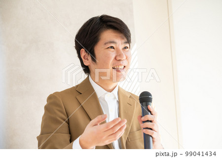 マイクを持って笑顔で話す若い男性 99041434