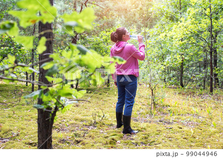 The girl drinks water in the forest on a summer sunny day. Survival in the forest, dehydration of the body. 99044946