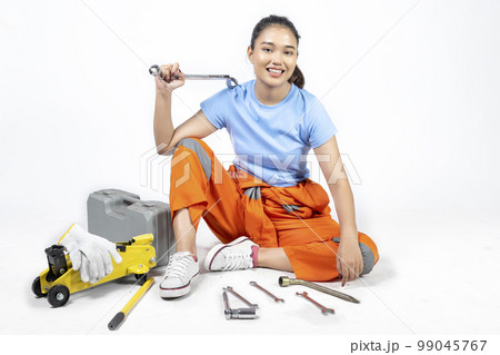 Asian woman car technician in uniform sitting with a car jack and toolkit box and wrench 99045767