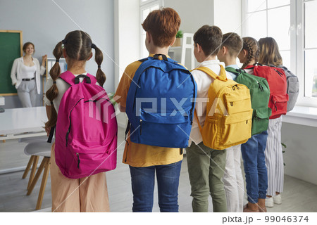 Back view of a group of school children with backpacks standing in the classroom 99046374