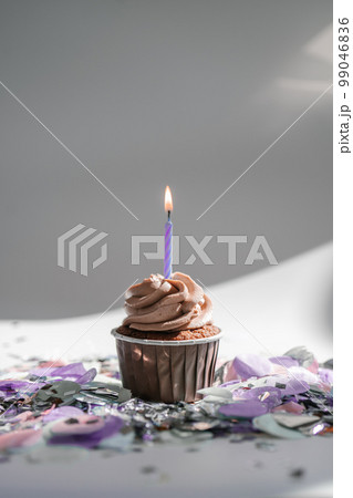 A cupcake with a candle stands on a white background with a shadow. 99046836