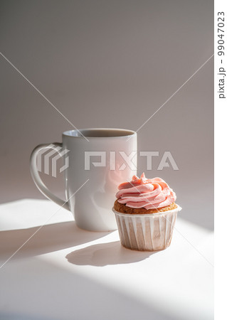 A cupcake or muffin stands next to a cup of coffee. A cupcake or muffin stands next to a cup of coffee. 99047023