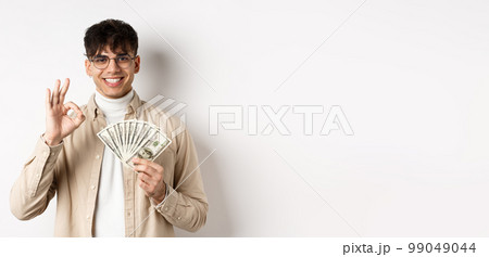 Handsome modern man in glasses showing dollar bills and okay gesture, making money, standing with cash on white background 99049044