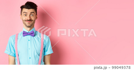 Smiling caucasian man looking excited, standing in classy bow-tie and shirt for romantic date, pink background 99049378