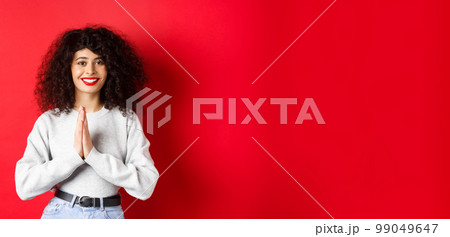 Beautiful smiling italian woman saying thank you, holding hands in namaste gesture and looking at camera grateful, standing on red background 99049647