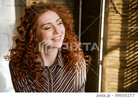Portrait of happy redhead young woman near window 99050257