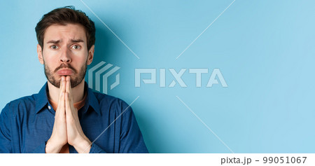 Sad young man begging for help, apoligizing and sobbing miserable, standing on blue background 99051067