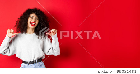 Confident young woman with red lips, pointing at herself and self-promoting, show-off while standing on red background Confident young woman with red lips, pointing at herself and self-promoting, show-off while standing on red background 99051481