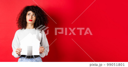Real estate. Sad woman dreaming of buying apartment, holding paper house cutout and looking up distressed, standing on red background Real estate. Sad woman dreaming of buying apartment, holding paper house cutout and looking up distressed, standing on red background 99051801