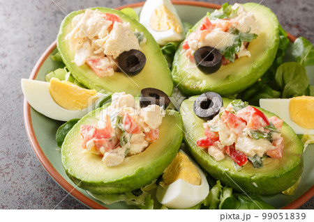 Chilean appetizer of ripe avocados stuffed with chicken salad on a bed of leafy greens close-up on a plate. Horizontal 99051839
