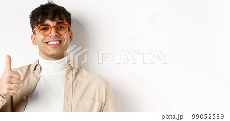 Handsome modern guy in glasses and earring, smiling satisfied and show thumb up, recommend company, standing on white background Handsome modern guy in glasses and earring, smiling satisfied and show thumb up, recommend company, standing on white background 99052539