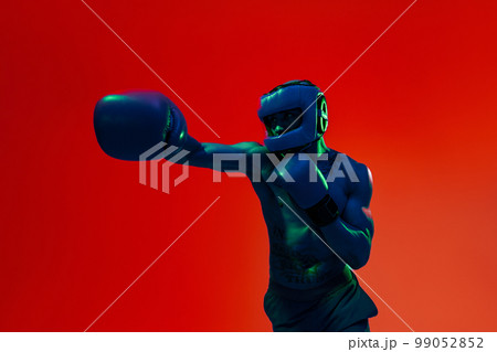 Sporty man wearing head guard and boxing gloves practicing for fight on studio background Sporty man wearing head guard and boxing gloves practicing for fight on studio background 99052852
