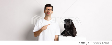 Sad and gloomy pet owner pointing at his black pug dog and sobbing, standing upster against white background 99053268