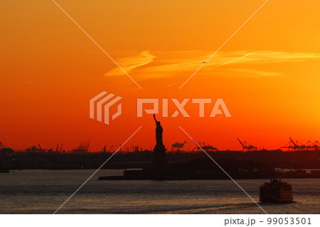 Silhouette of Statue of Liberty and Liberty Island in New York against an orange sunset sky Silhouette of Statue of Liberty and Liberty Island in New York against an orange sunset sky 99053501