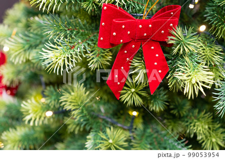Decorated Christmas Tree, Red Bow, Shiny Garland on Green Branches, Blurred Background 99053954