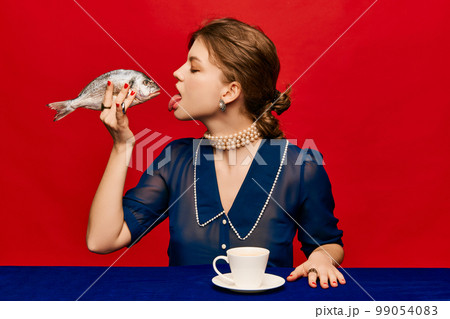 Tasting new taste. Young extravagant woman with cup of coffee and raw fish on bright red background. Vintage, retro style. Complementary colors. Food pop art photography. Tasting new taste. Young extravagant woman with cup of coffee and raw fish on bright red background. Vintage, retro style. Complementary colors. Food pop art photography. 99054083