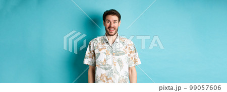 Summer holiday. Handsome happy man in hawaiian shirt looking amused, smiling at camera, standing on blue background Summer holiday. Handsome happy man in hawaiian shirt looking amused, smiling at camera, standing on blue background 99057606