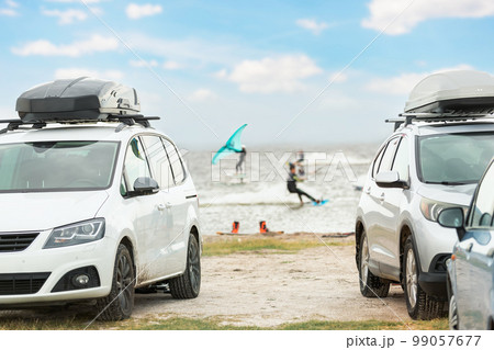 Front view many cars parked with surf board kite equipment on sand beach, van vehicle with rooftop box ocean sea beach watersport spot camp. Adventure travel water sport acitivity 99057677
