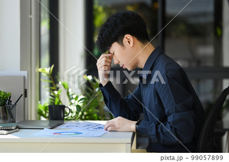 Tired asian male office worker holding her head in hands, exhausted from overwork or stress at work 99057899