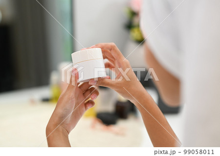 Over shoulder view of woman holding jar with moisturizing cream. Home care, Beauty treatment concept 99058011