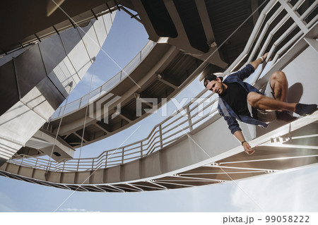 Freerunning athlete is hanging on the bridge and getting ready for a dangerous jump Freerunning athlete is hanging on the bridge and getting ready for a dangerous jump 99058222