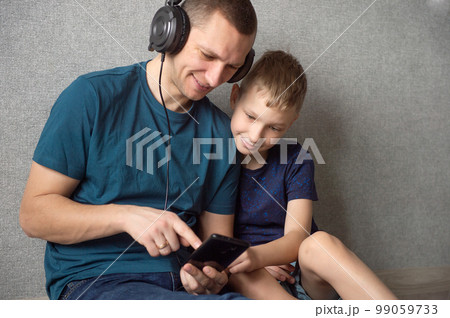 Dad is sitting on the floor next to his son with headphones on and pointing into the phone Dad is sitting on the floor next to his son with headphones on and pointing into the phone 99059733