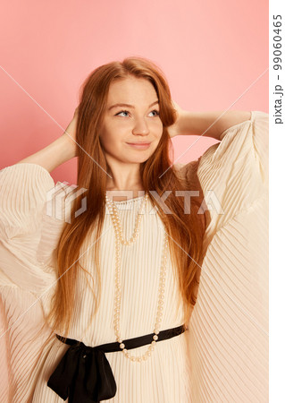 One young beautiful redhaired girl with long hair posing isolated over light pink background. Concept of positive emotions, happy mood, fashion, youth 99060465
