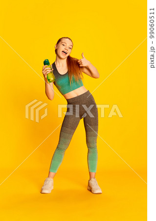 Emotional beautiful girl in sports fitness clothes doing exercises with dumbbells over yellow background. Sport, fitness, happy positive emotions and active lifestyle concept. Emotional beautiful girl in sports fitness clothes doing exercises with dumbbells over yellow background. Sport, fitness, happy positive emotions and active lifestyle concept. 99060511