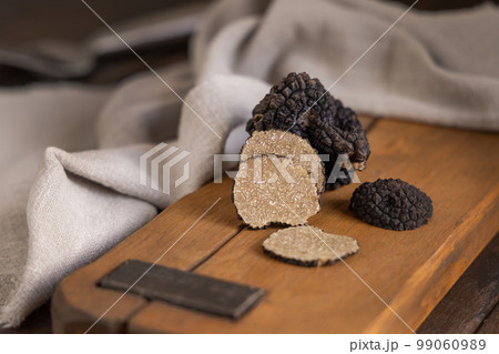 Whole and sliced black truffles mushroom on wooden board on dark brown table, close up Whole and sliced black truffles mushroom on wooden board on dark brown table, close up 99060989