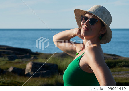 Woman tourist in a straw hat and a green dress on the seashore on a bright sunny day Woman tourist in a straw hat and a green dress on the seashore on a bright sunny day 99061419