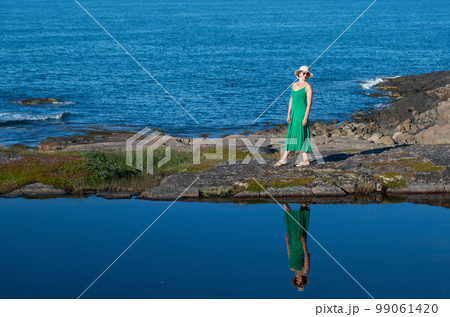 Woman tourist in a straw hat and a green dress on the seashore on a bright sunny day Woman tourist in a straw hat and a green dress on the seashore on a bright sunny day 99061420