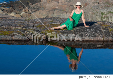 Woman tourist in a straw hat and a green dress on the seashore on a bright sunny day 99061421