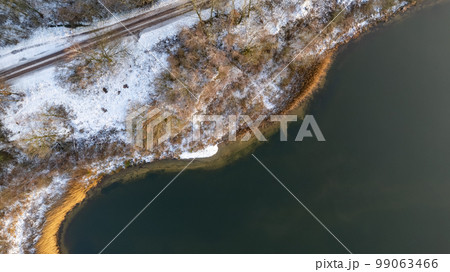 Aerial view of the winter snow covered forest and frozen lake from above captured with a drone. High Aerial view of the winter snow covered forest and frozen lake from above captured with a drone. High 99063466