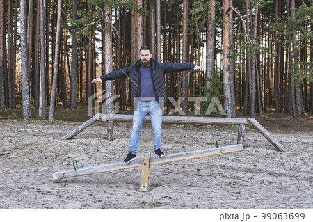 Adult bearded man hipster staying on swing at a play area in the forest. Concept of sanity, harmony and balance Adult bearded man hipster staying on swing at a play area in the forest. Concept of sanity, harmony and balance 99063699