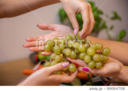 Close-up on the hands of two women handing each other a bunch of grapes Close-up on the hands of two women handing each other a bunch of grapes 99064708