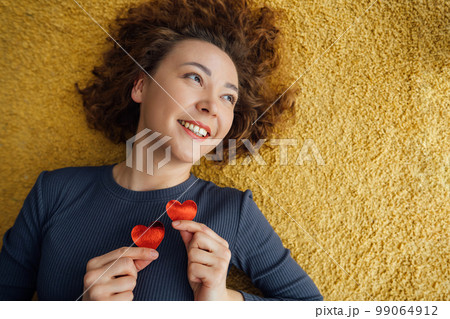 Joyful woman holding two cardboard hearts near chest Top view, yellow background 99064912