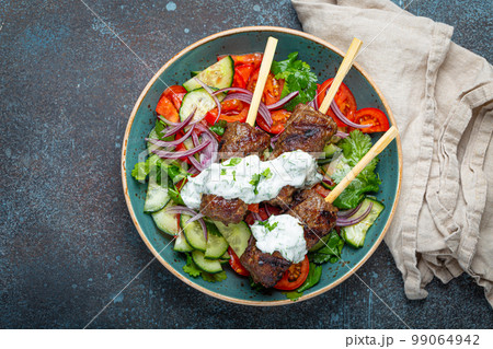 Grilled skewer meat beef kebabs on sticks served with fresh vegetables salad on plate on rustic concrete background from above. Traditional Middle Eastern, Turkish dish Kebab 99064942