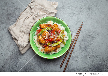 Asian sweet and sour sticky chicken with vegetables stir-fry and rice in ceramic bowl with chopsticks top view, gray rustic stone background, traditional Asian dish Asian sweet and sour sticky chicken with vegetables stir-fry and rice in ceramic bowl with chopsticks top view, gray rustic stone background, traditional Asian dish 99064956