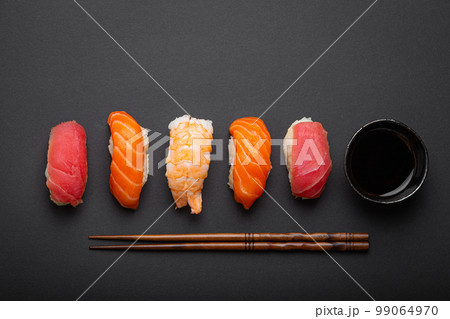 Traditional Japanese sushi top view with soy sauce and chopsticks on dark black minimal background. Sushi with salmon, tuna, shrimp, space for text 99064970