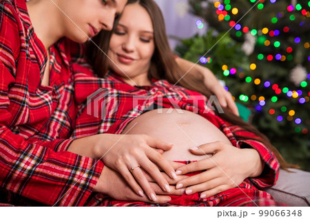 A man hugs a pregnant woman with her exposed belly in the foreground. A man hugs a pregnant woman with her exposed belly in the foreground. 99066348