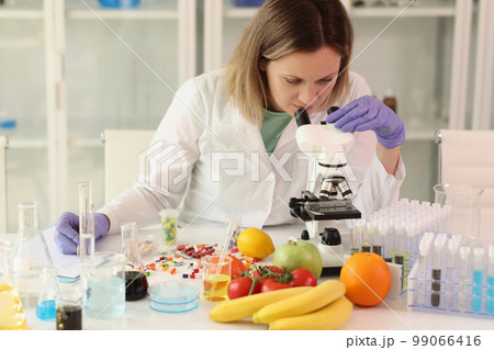 Female scientist with microscope, test tubes, laboratory glassware and reagents examining food. 99066416