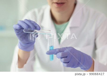 Gloved female scientist holds two test tubes of liquid in her hands close-up. 99066427